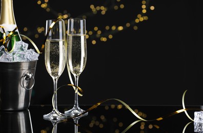 Photo of Champagne and bucket of ice on mirror surface against black background with blurred lights, space for text