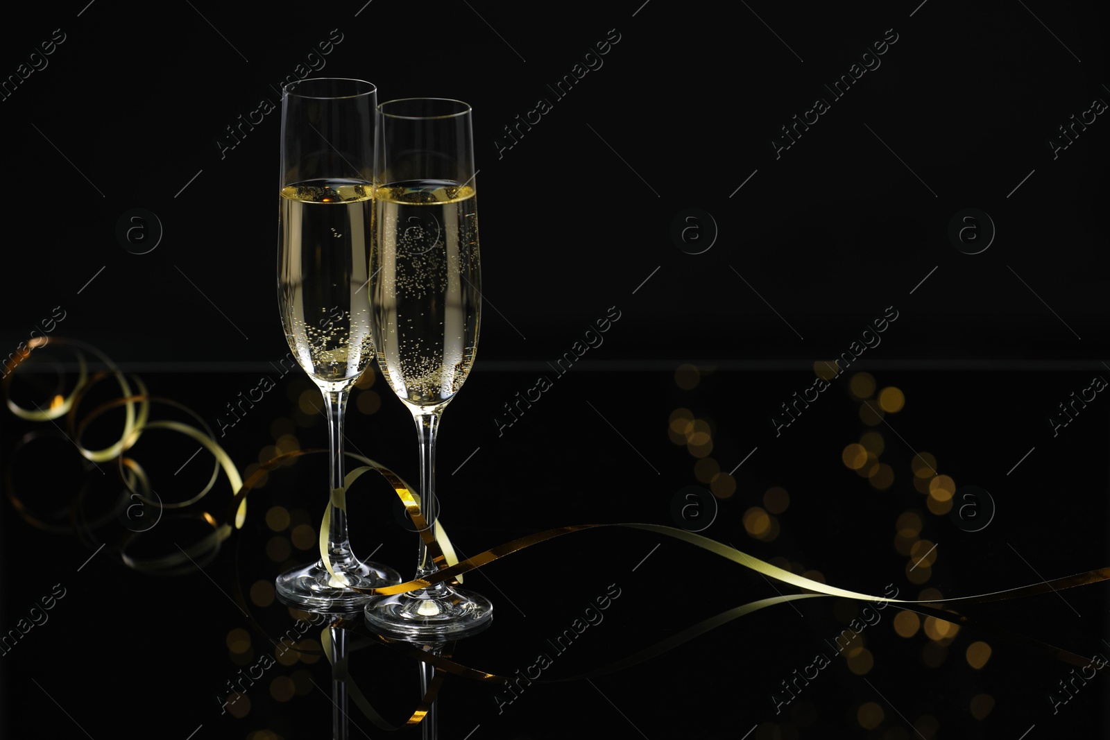 Photo of Champagne in glasses and party streamers on black mirror surface, space for text