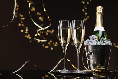 Photo of Champagne and bucket of ice on mirror surface against brown background with blurred lights, space for text