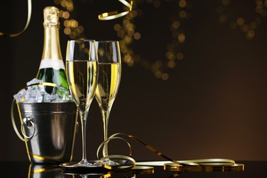 Photo of Champagne and bucket of ice on mirror surface against brown background with blurred lights, space for text