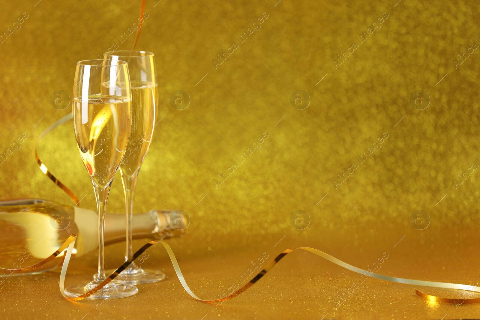 Photo of Champagne in glasses and bottle on golden background. Space for text