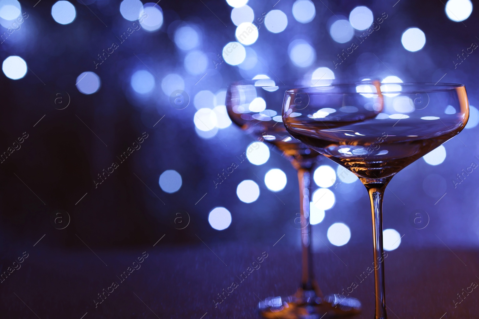 Photo of Champagne in glasses on table against blurred lights, closeup. Space for text