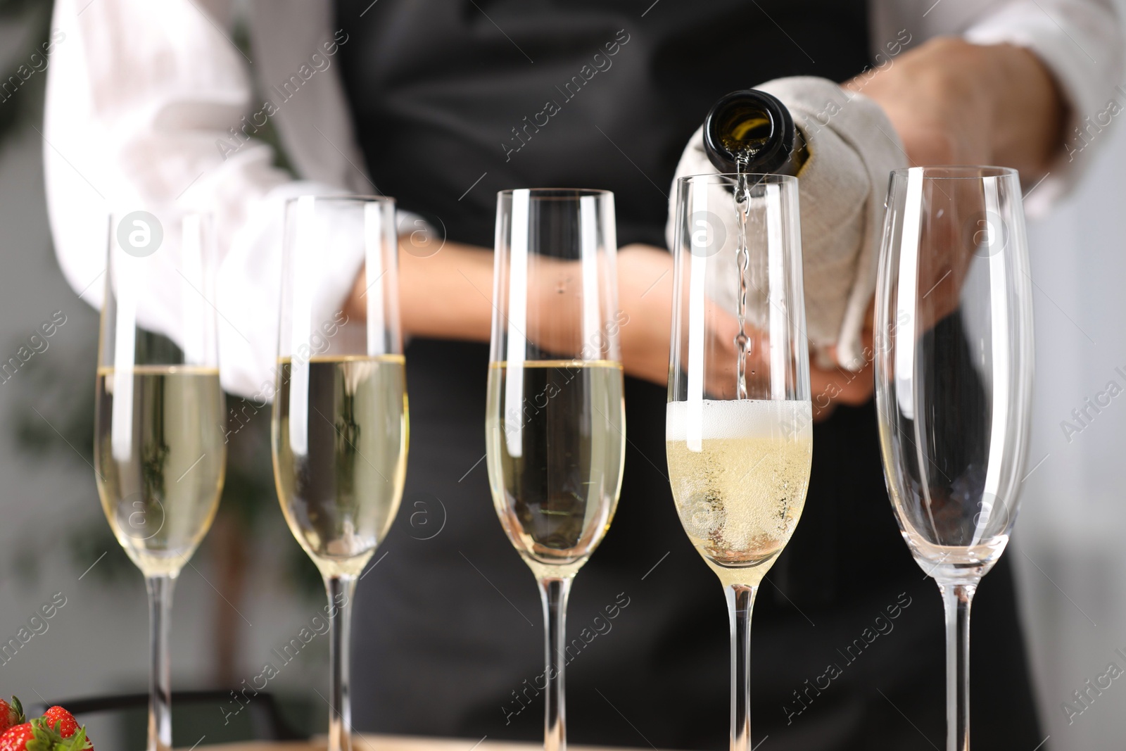 Photo of Waiter filling glasses with champagne indoors, closeup