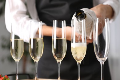 Photo of Waiter filling glasses with champagne indoors, closeup