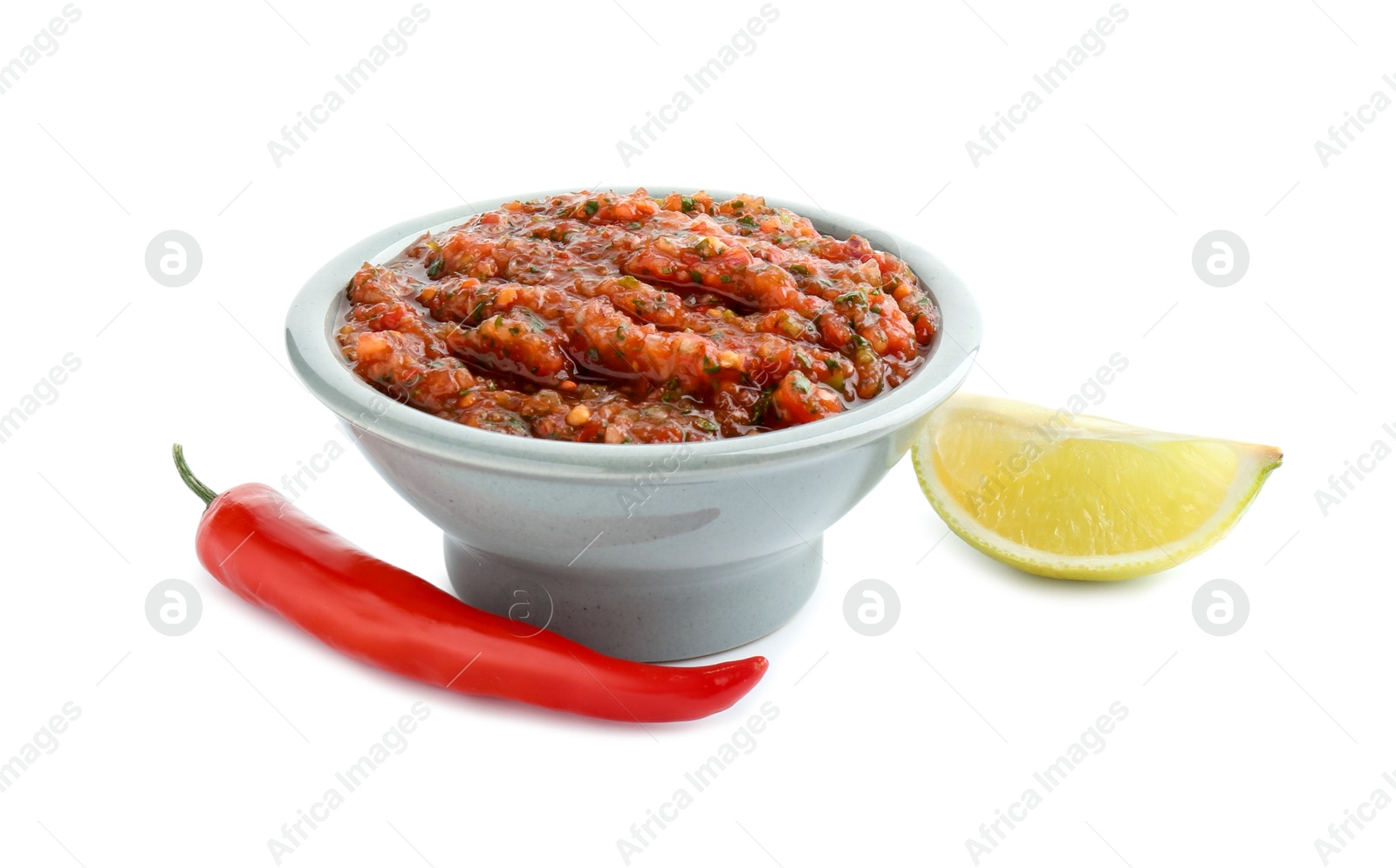 Photo of Tasty salsa sauce in bowl, lime and chili pepper isolated on white