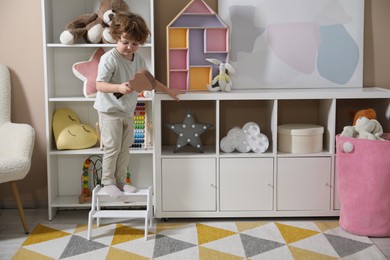 Photo of Little boy with toy guitar standing on step stool at home