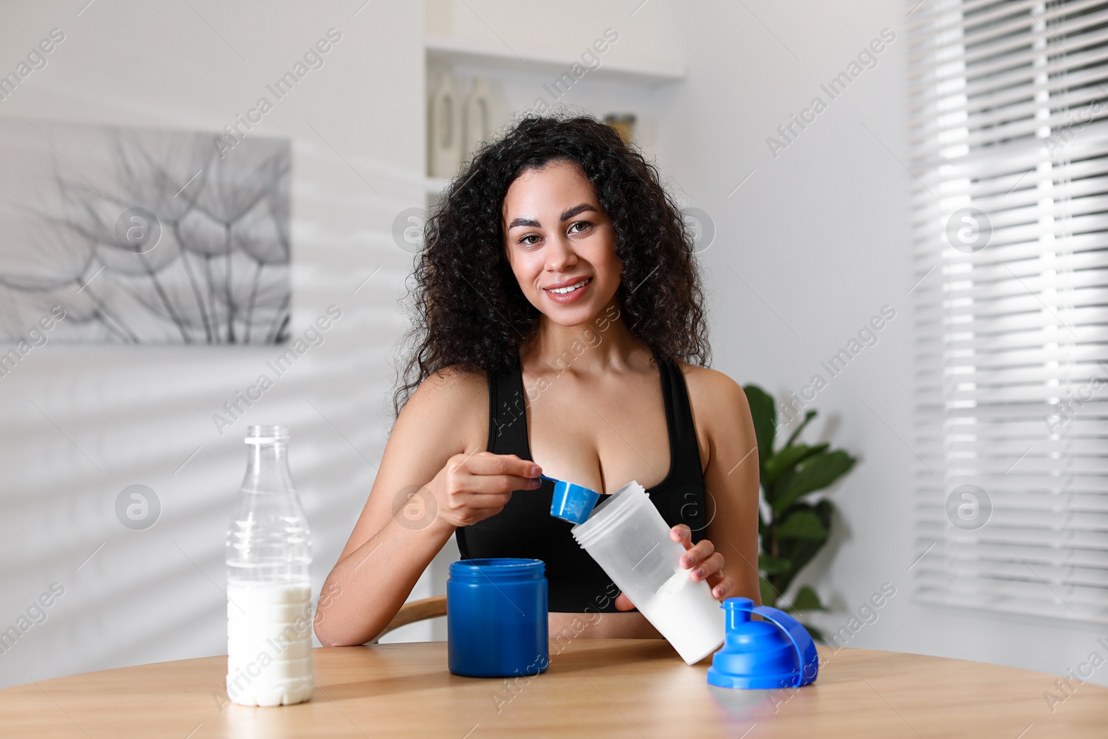 Photo of Beautiful woman making protein shake at wooden table indoors