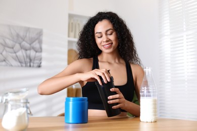 Photo of Beautiful woman making protein shake at wooden table indoors