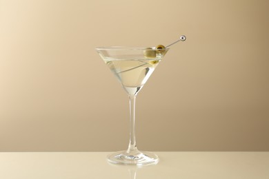 Photo of Martini cocktail with olives in glass on beige table