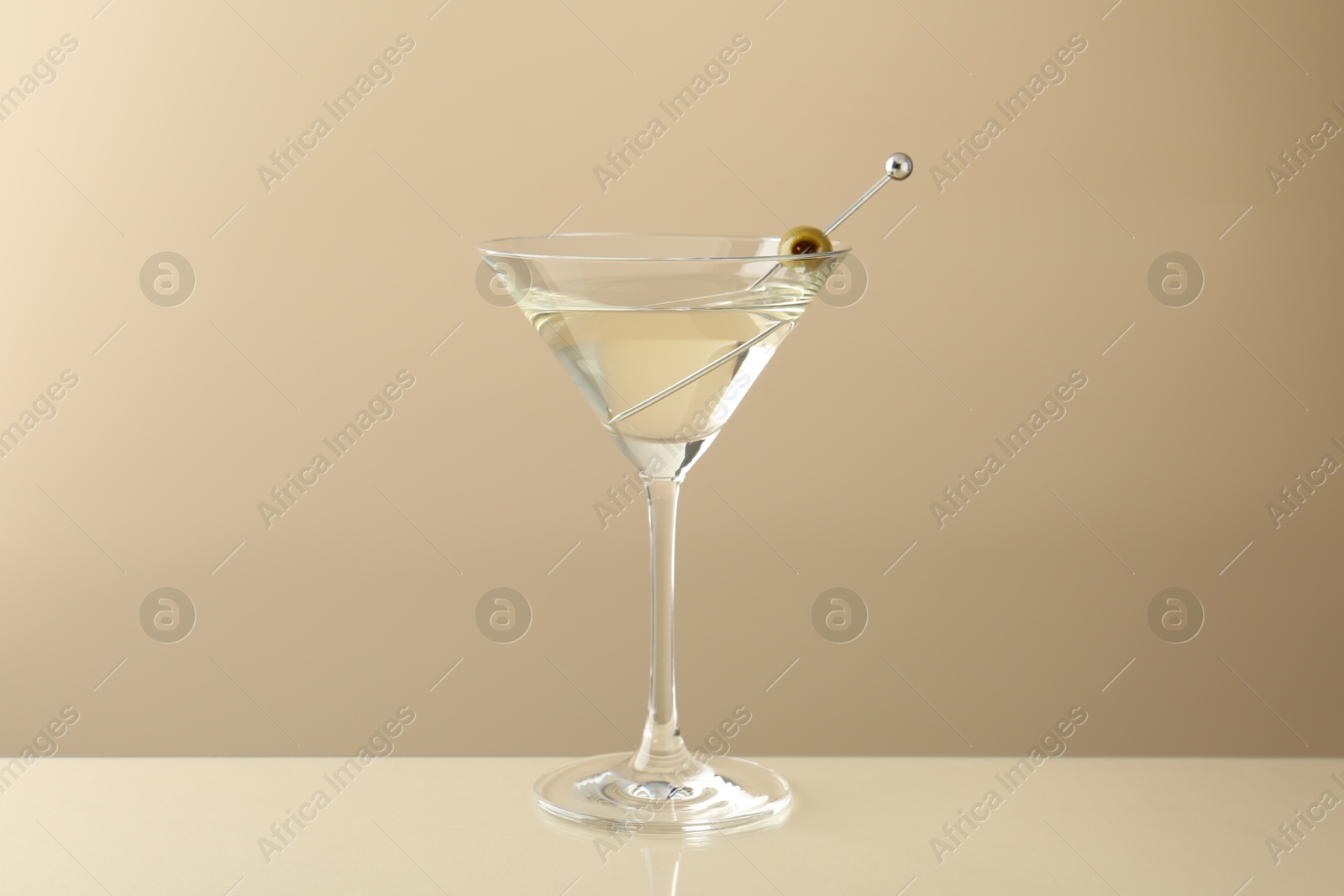 Photo of Martini cocktail with olive in glass on beige table