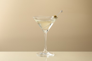 Photo of Martini cocktail with olive in glass on beige table