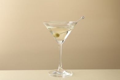 Photo of Martini cocktail with olive in glass on beige table