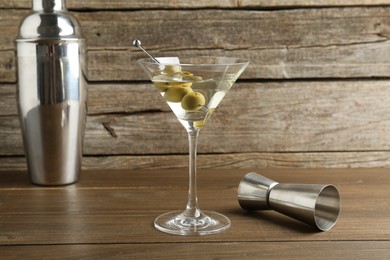 Martini cocktail with olives in glass, shaker and jigger on wooden table