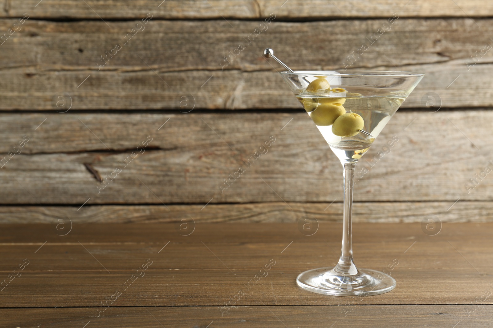 Photo of Martini cocktail with olives in glass on wooden table, space for text