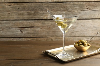 Photo of Martini cocktail in glass with olives on wooden table, space for text