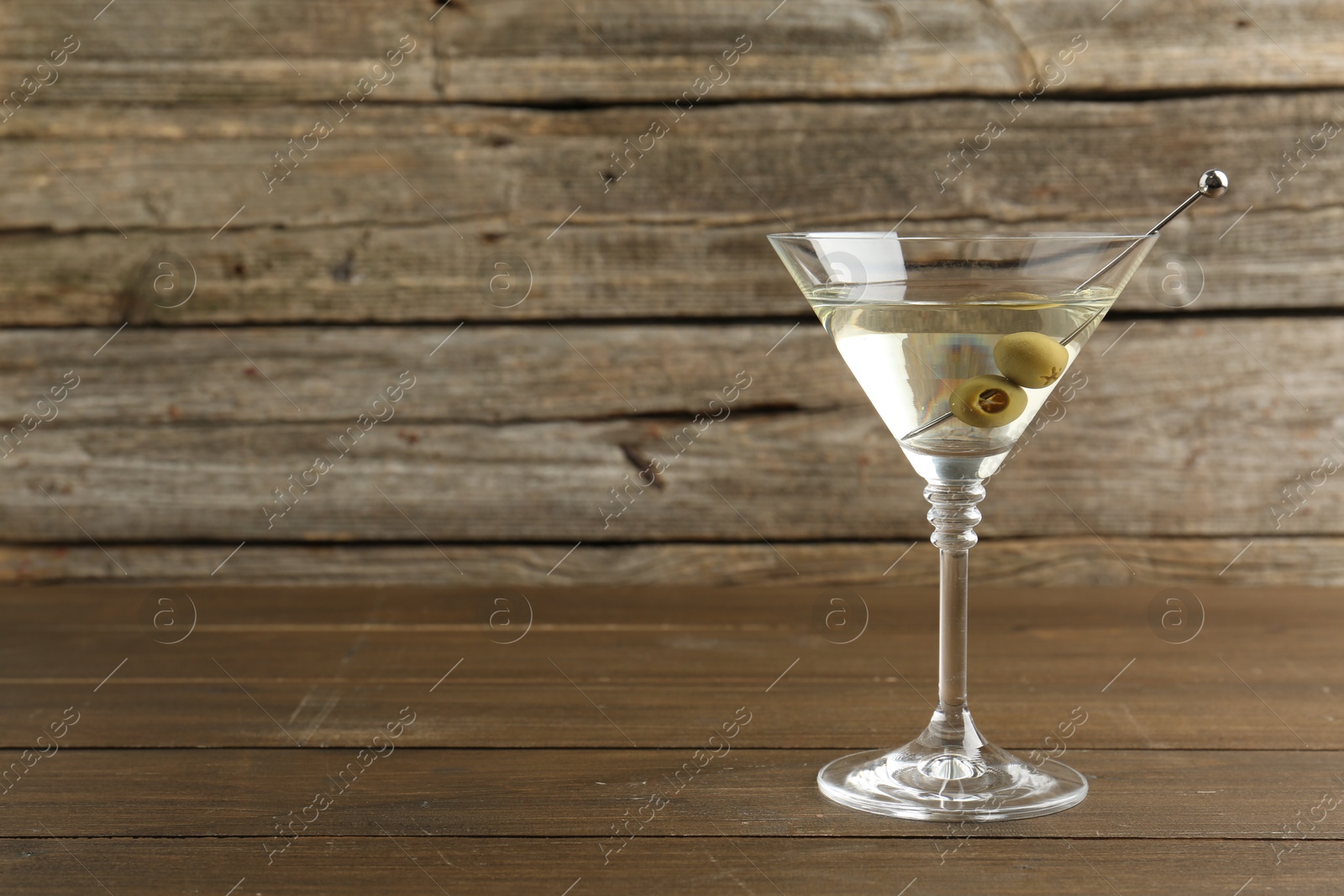 Photo of Martini cocktail with olives in glass on wooden table, space for text