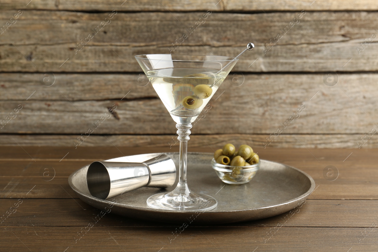 Photo of Martini cocktail in glass with olives and jigger on wooden table