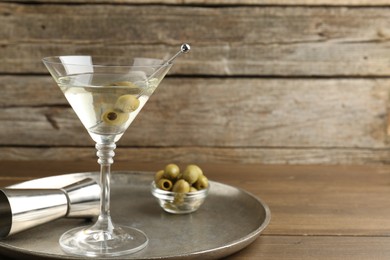 Photo of Martini cocktail in glass with olives and jigger on wooden table, space for text