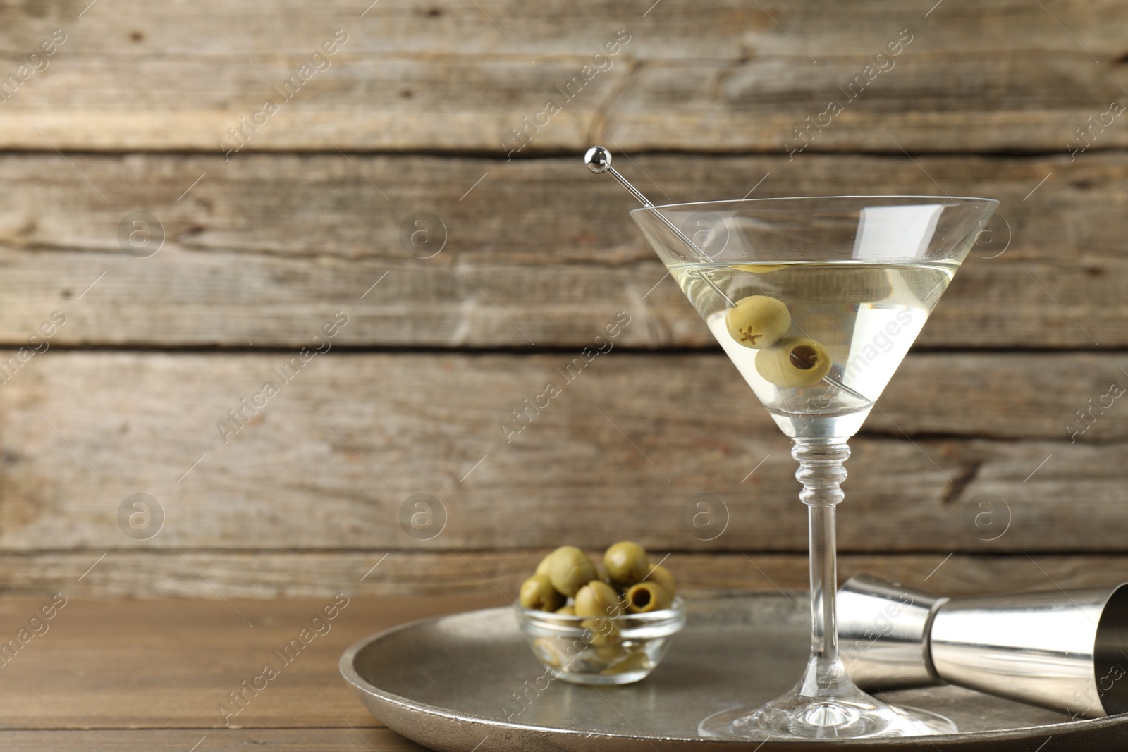 Photo of Martini cocktail in glass with olives and jigger on wooden table, space for text