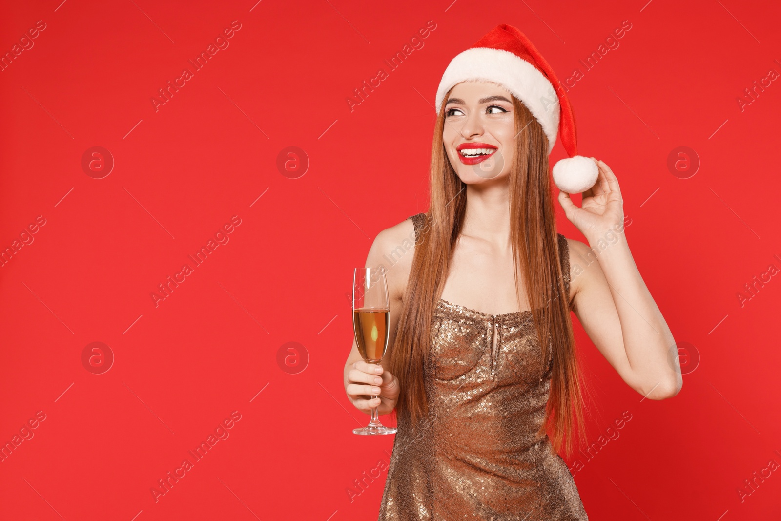 Photo of Young woman in Santa hat with glass of wine on red background, space for text. Christmas celebration