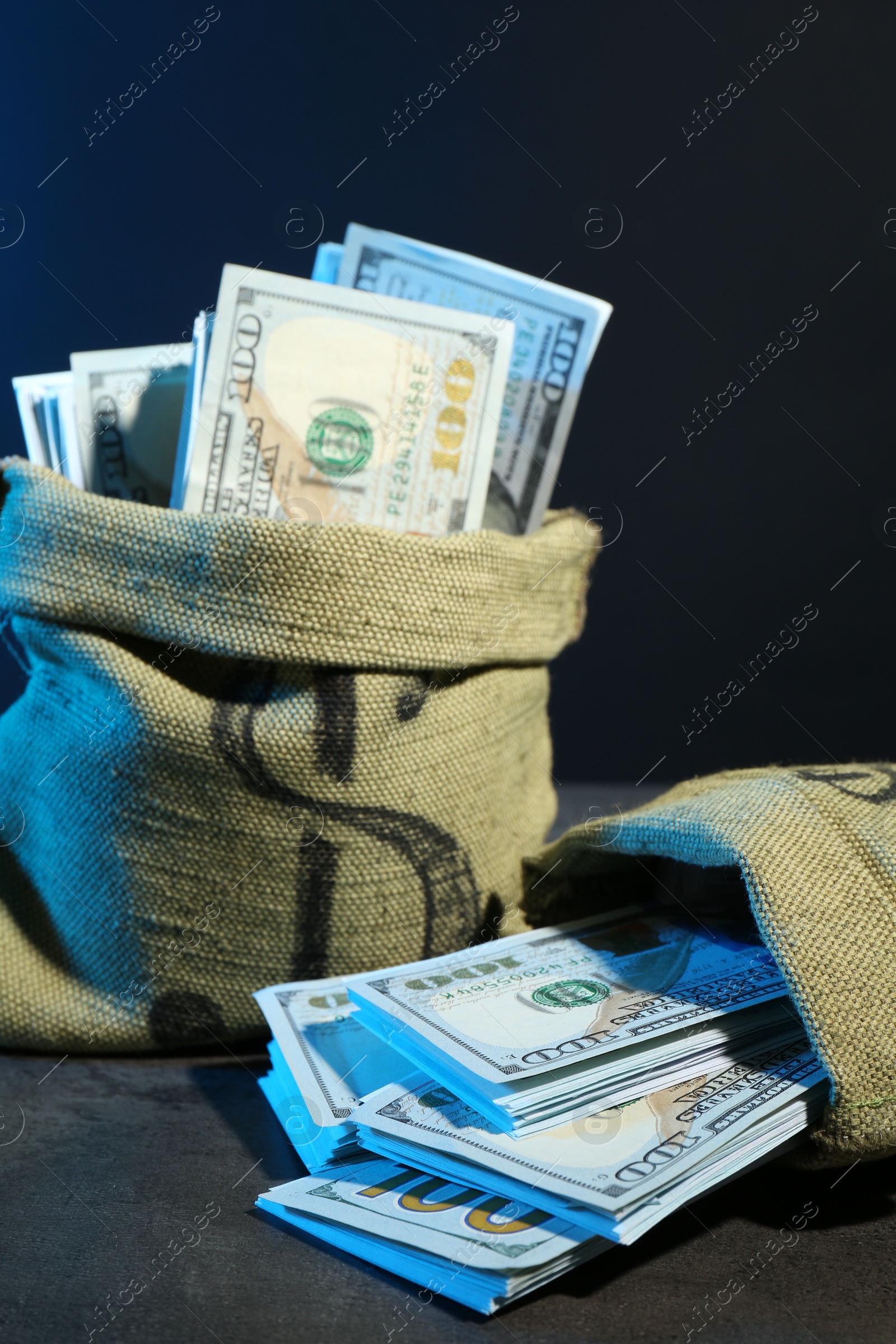 Photo of Dollar banknotes in burlap sacks on grey table against dark background in neon lights