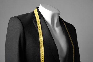 Photo of Male mannequin with black jacket and measuring tape on grey background, closeup