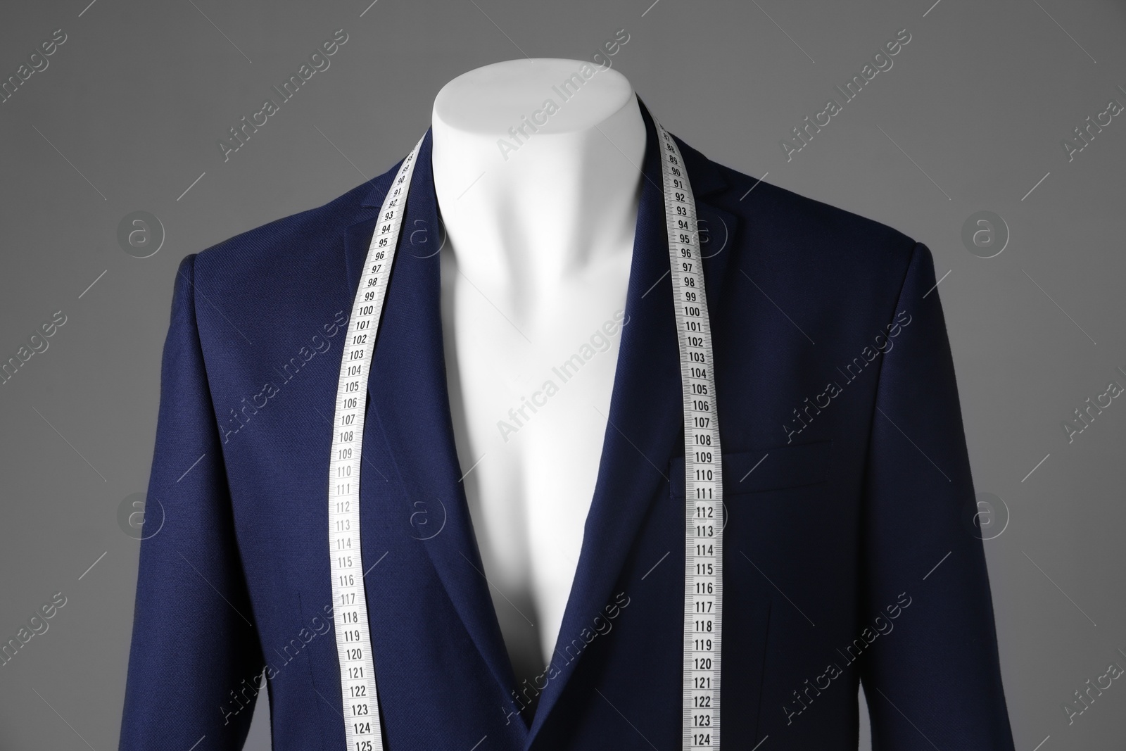 Photo of Male mannequin with blue jacket and measuring tape on grey background, closeup