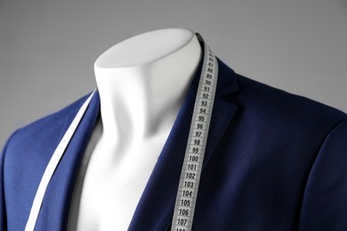 Photo of Male mannequin with blue jacket and measuring tape on grey background, closeup