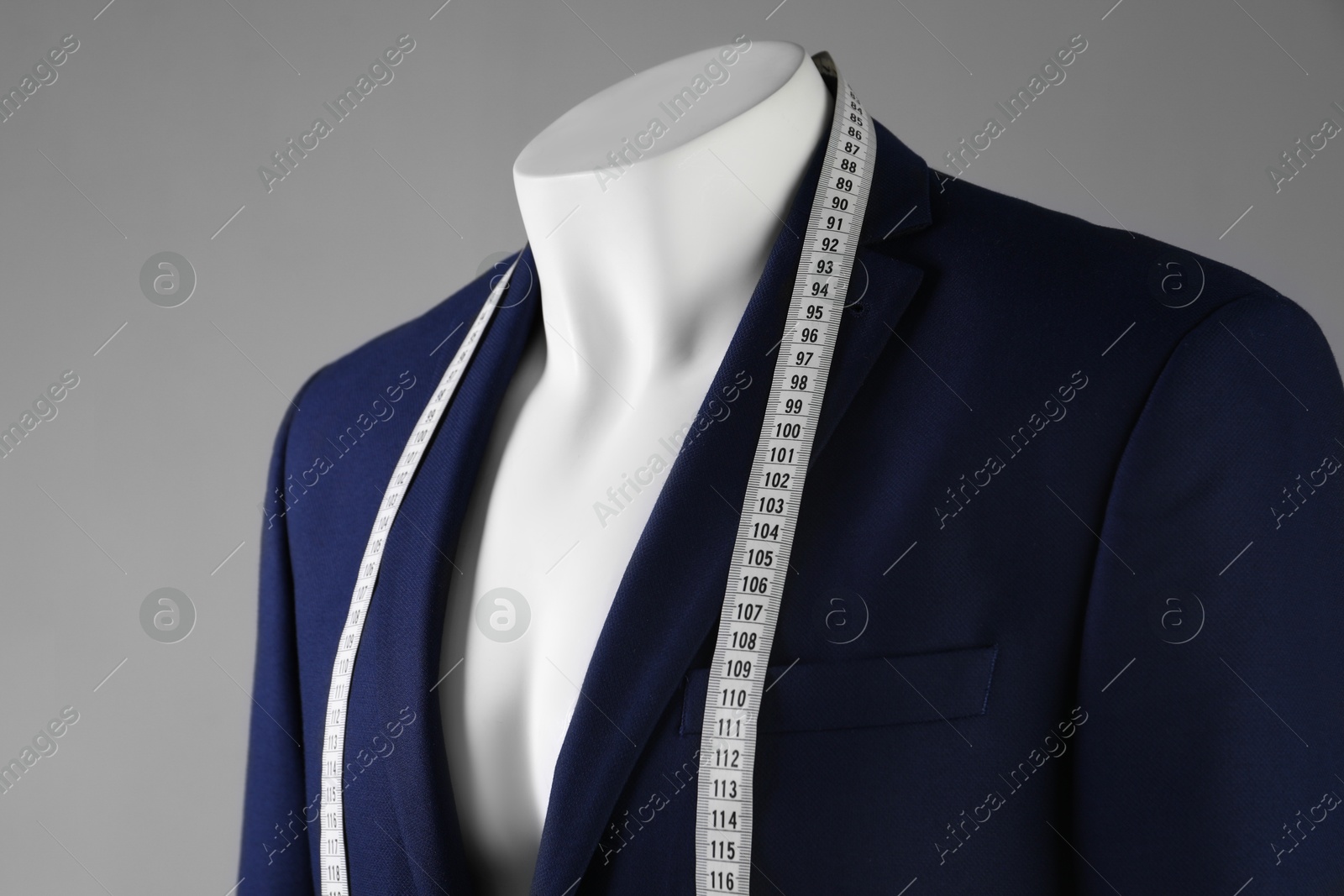 Photo of Male mannequin with blue jacket and measuring tape on grey background, closeup