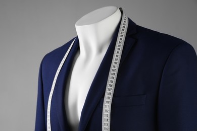 Photo of Male mannequin with blue jacket and measuring tape on grey background, closeup