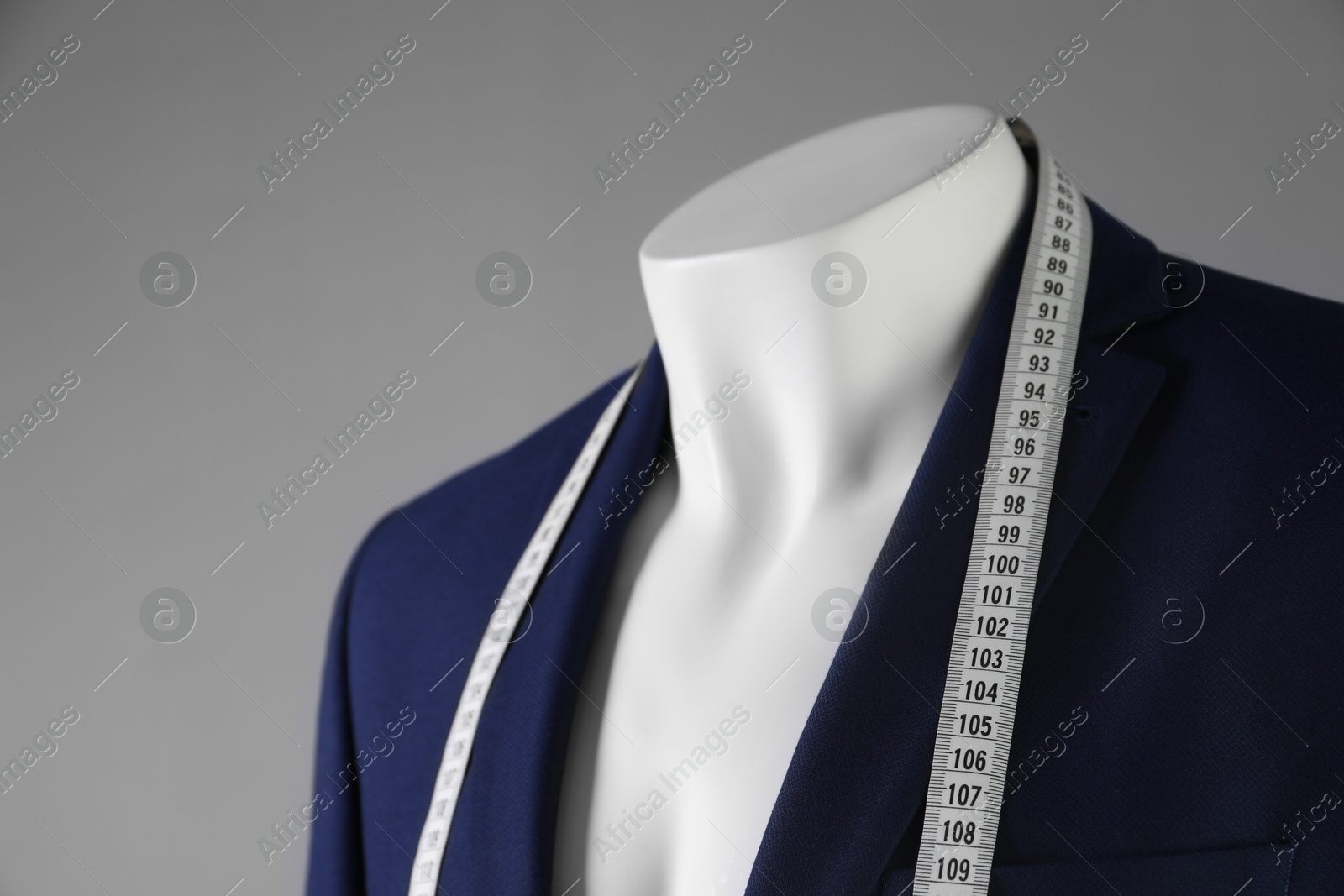 Photo of Male mannequin with blue jacket and measuring tape on grey background, closeup