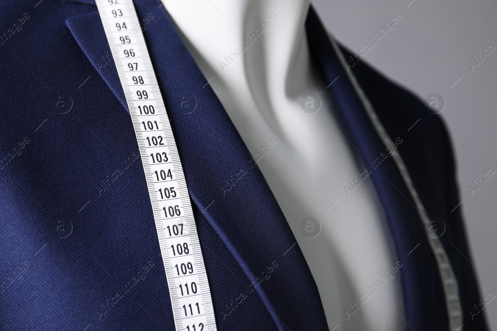 Photo of Male mannequin with blue jacket and measuring tape on grey background, closeup