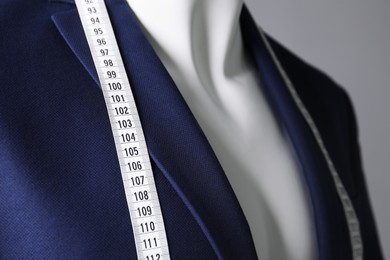 Photo of Male mannequin with blue jacket and measuring tape on grey background, closeup