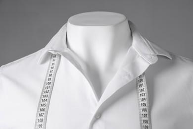 Male mannequin with white shirt and measuring tape on grey background, closeup