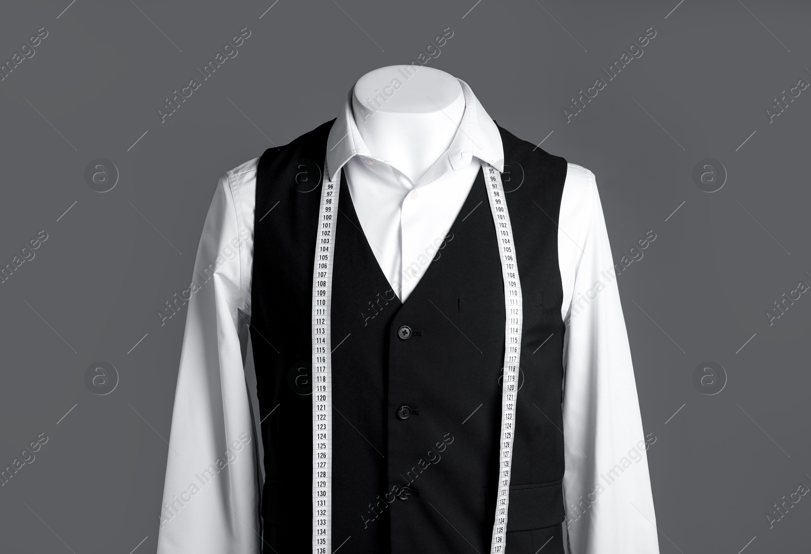 Photo of Male mannequin with black vest, white shirt and measuring tape on grey background