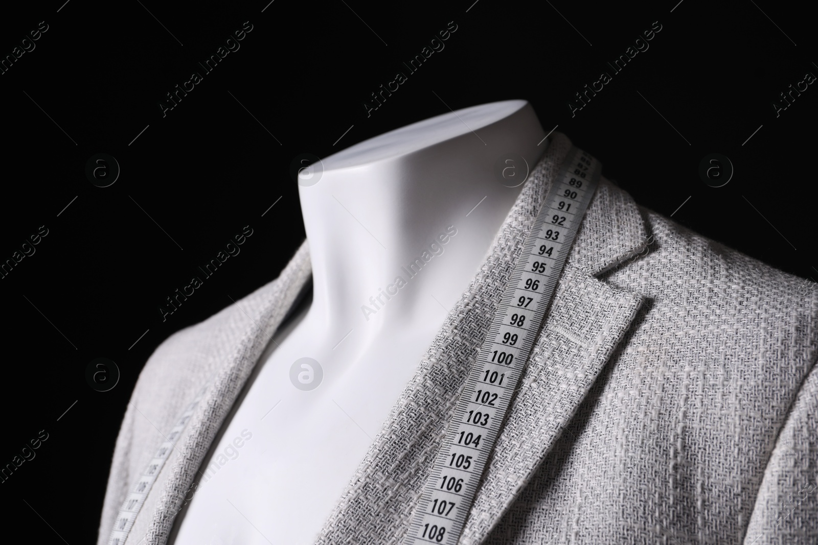 Photo of Male mannequin with grey jacket and measuring tape on black background, closeup