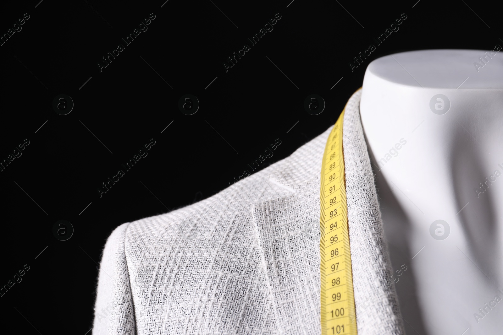 Photo of Male mannequin with grey jacket and measuring tape on black background, closeup