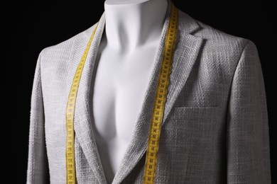 Male mannequin with grey jacket and measuring tape on black background, closeup