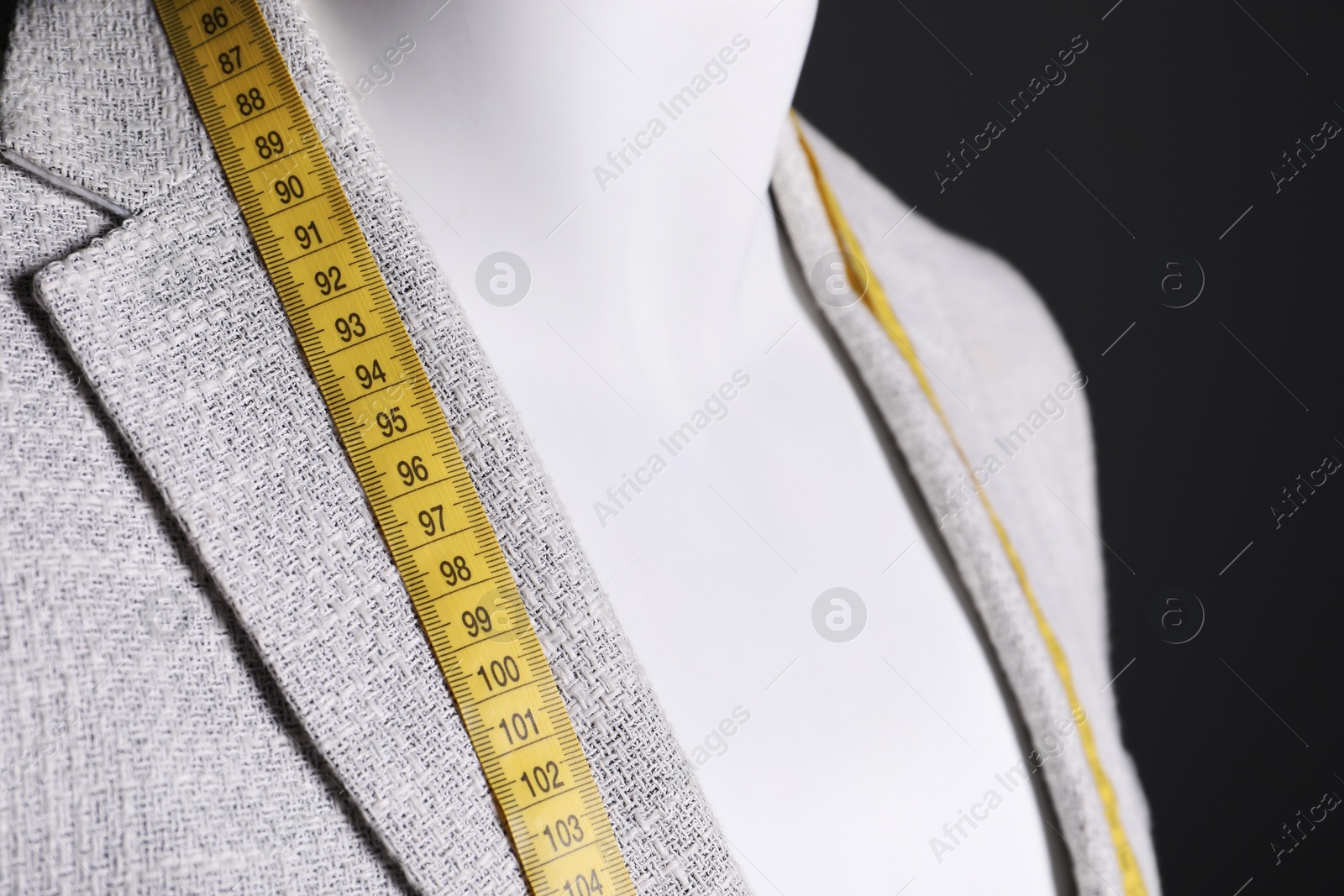 Photo of Male mannequin with grey jacket and measuring tape on black background, closeup