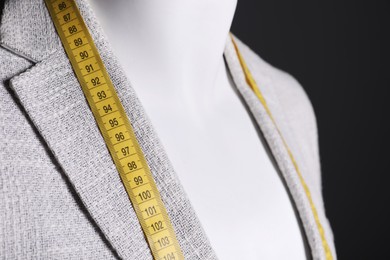 Photo of Male mannequin with grey jacket and measuring tape on black background, closeup