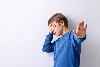 Photo of Scared little boy covering eyes on light background. Space for text