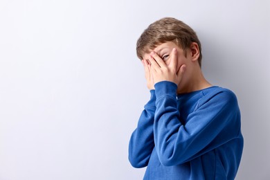 Photo of Scared little boy hiding on light background. Space for text