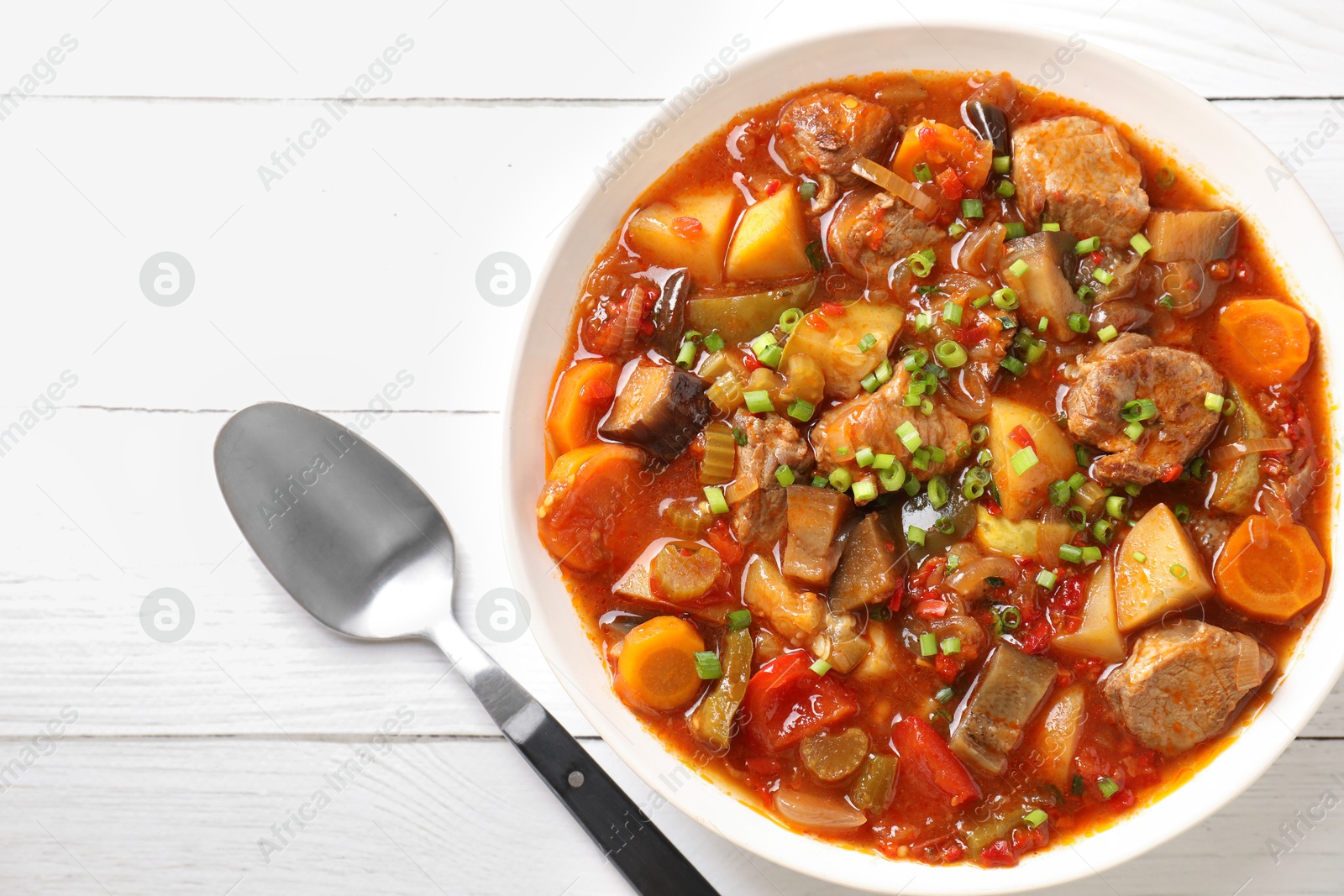 Photo of Delicious stew with vegetables in bowl and spoon on white wooden table, top view