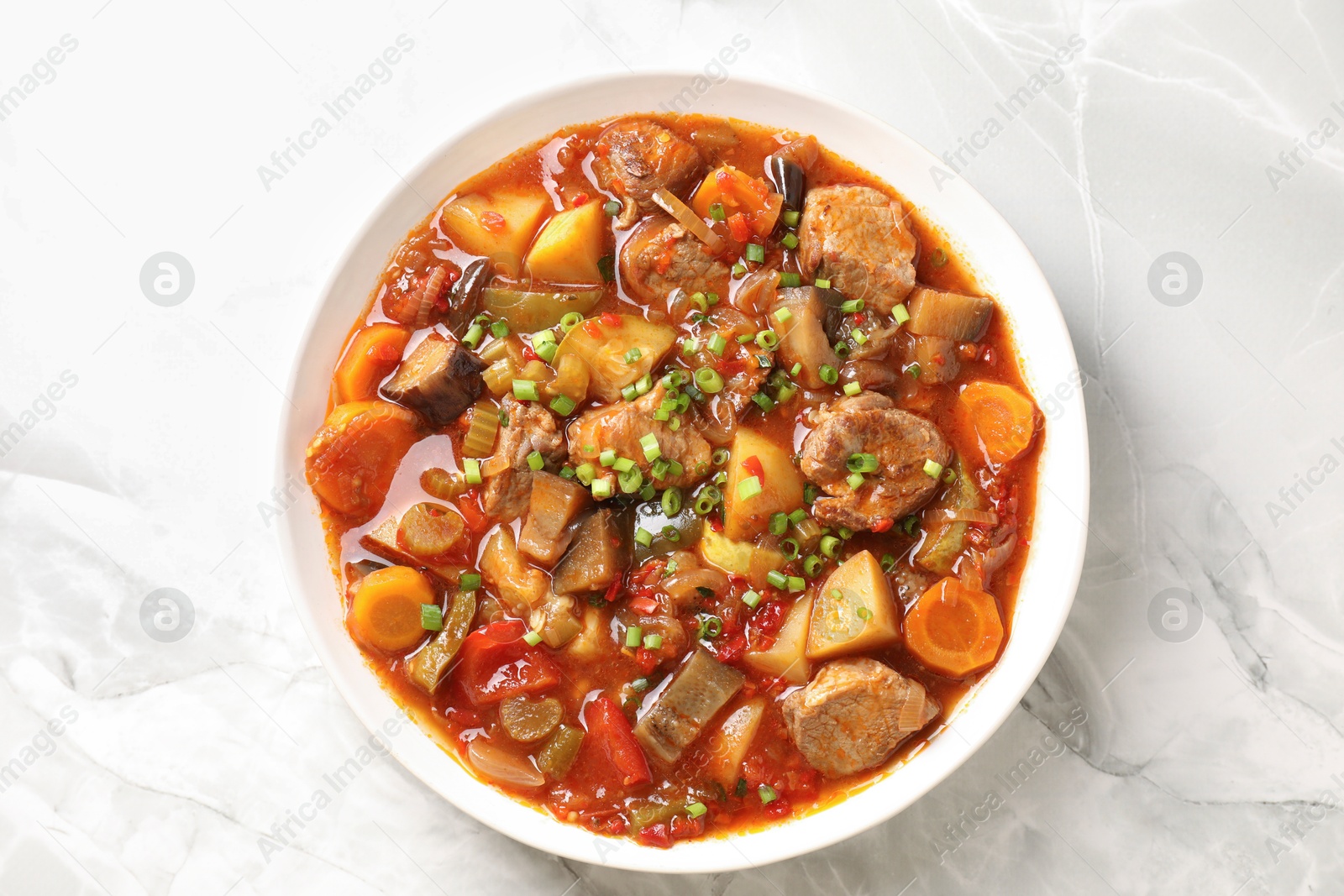 Photo of Delicious stew with vegetables in bowl on white marble table, top view