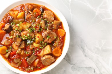 Photo of Delicious stew with vegetables in bowl on white marble table, top view. Space for text