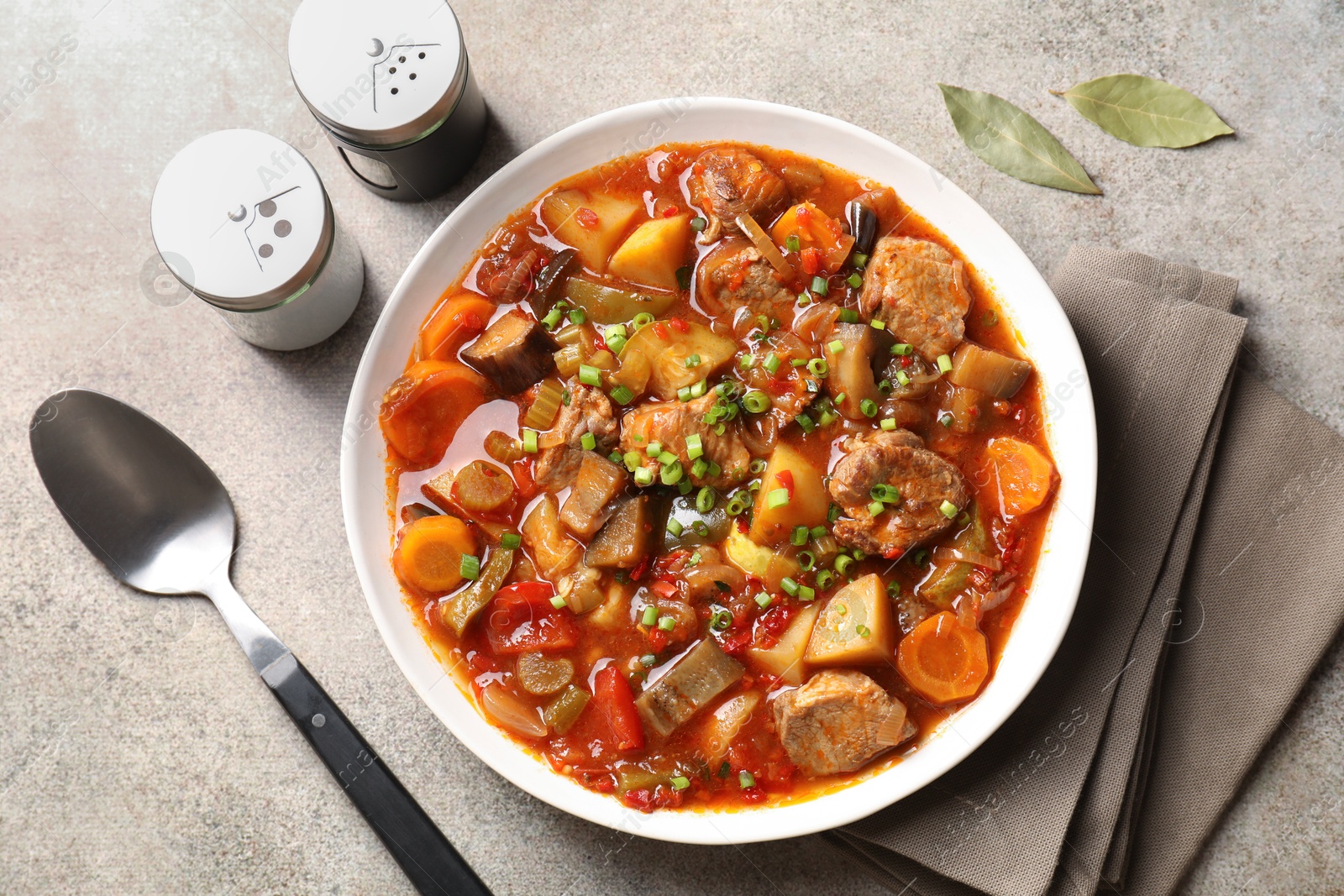 Photo of Delicious stew with vegetables in bowl, spices and spoon on light grey table, top view