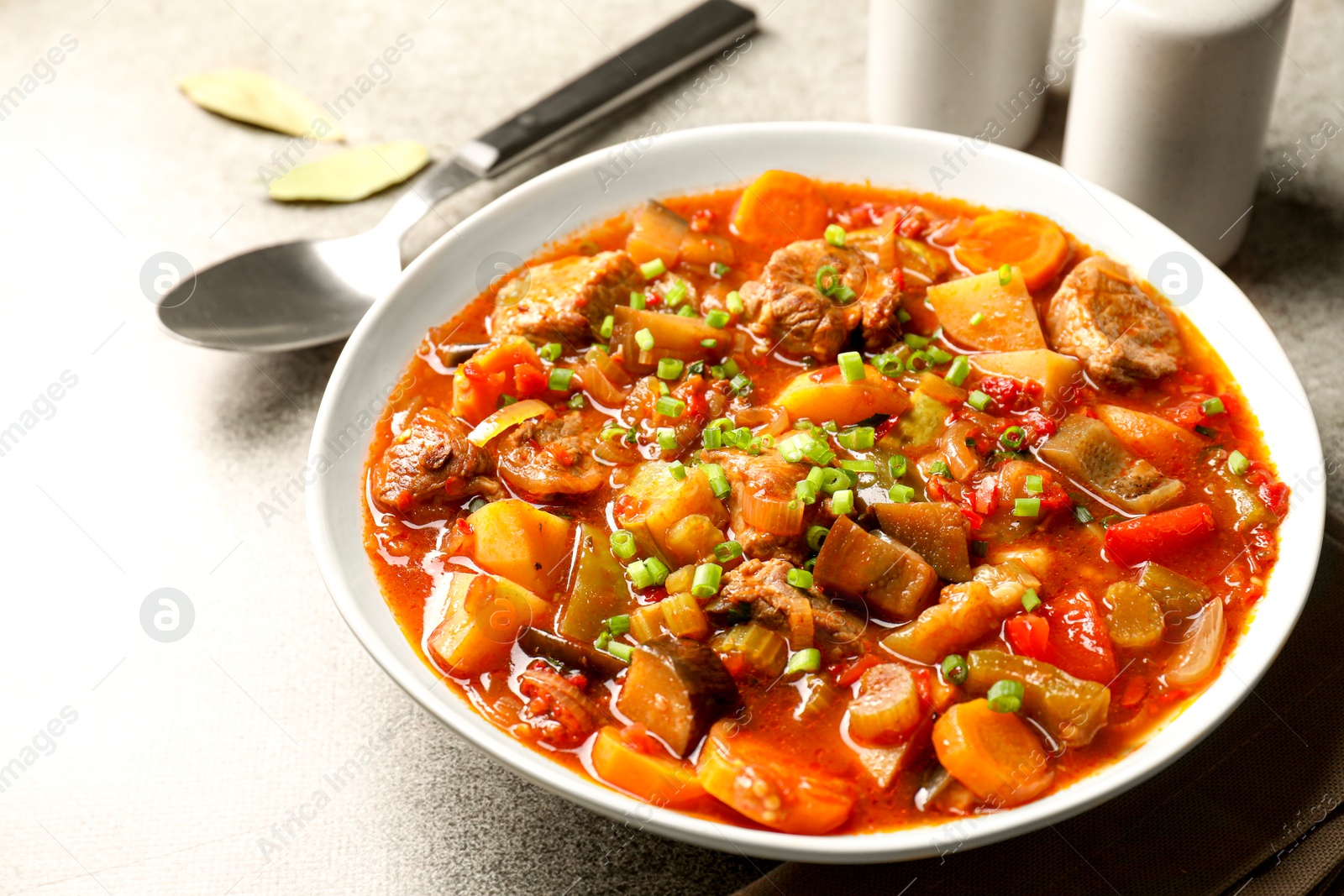 Photo of Delicious stew with vegetables in bowl on light grey table, closeup