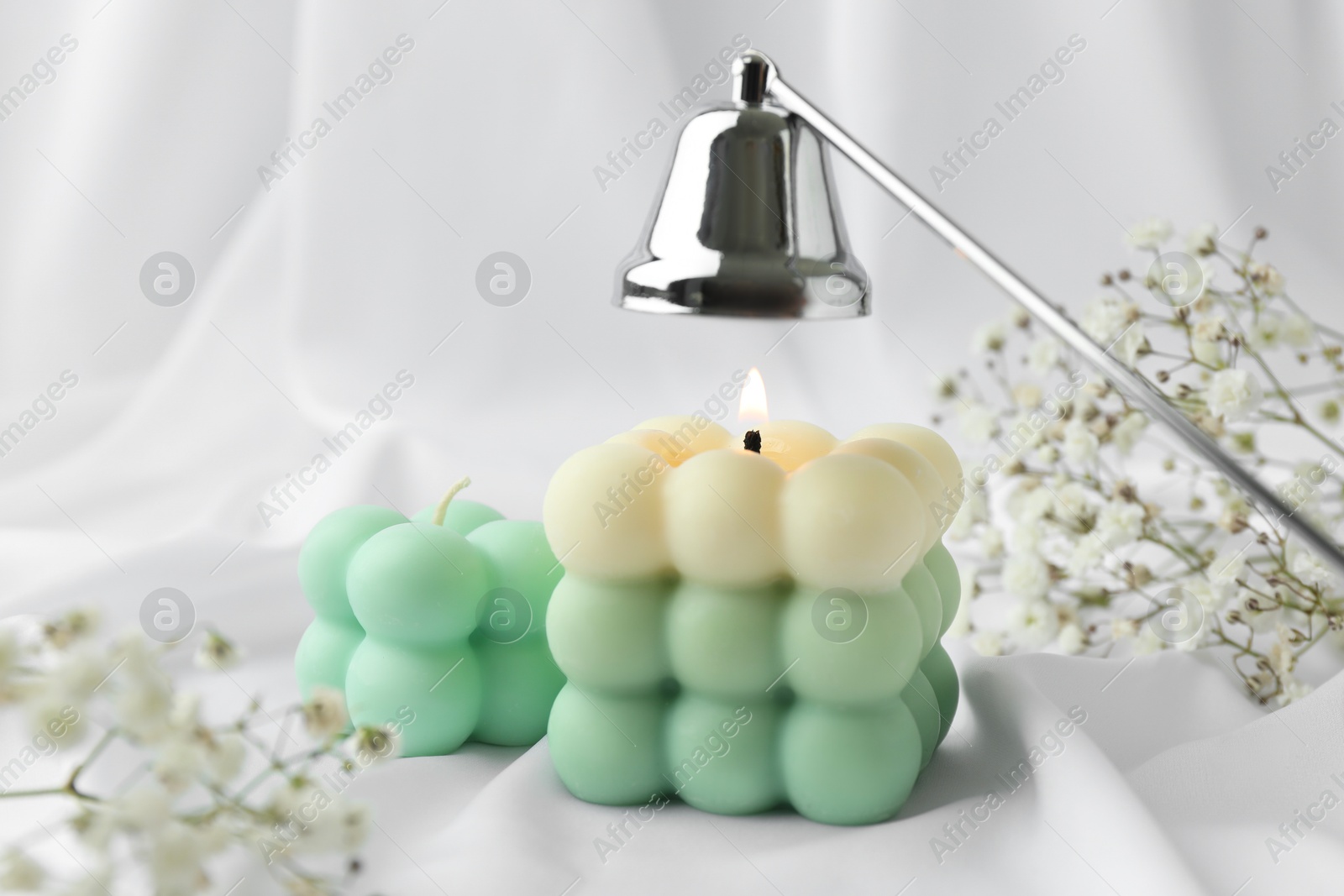 Photo of Stylish bubble candles, snuffer and gypsophila flowers on white cloth, closeup