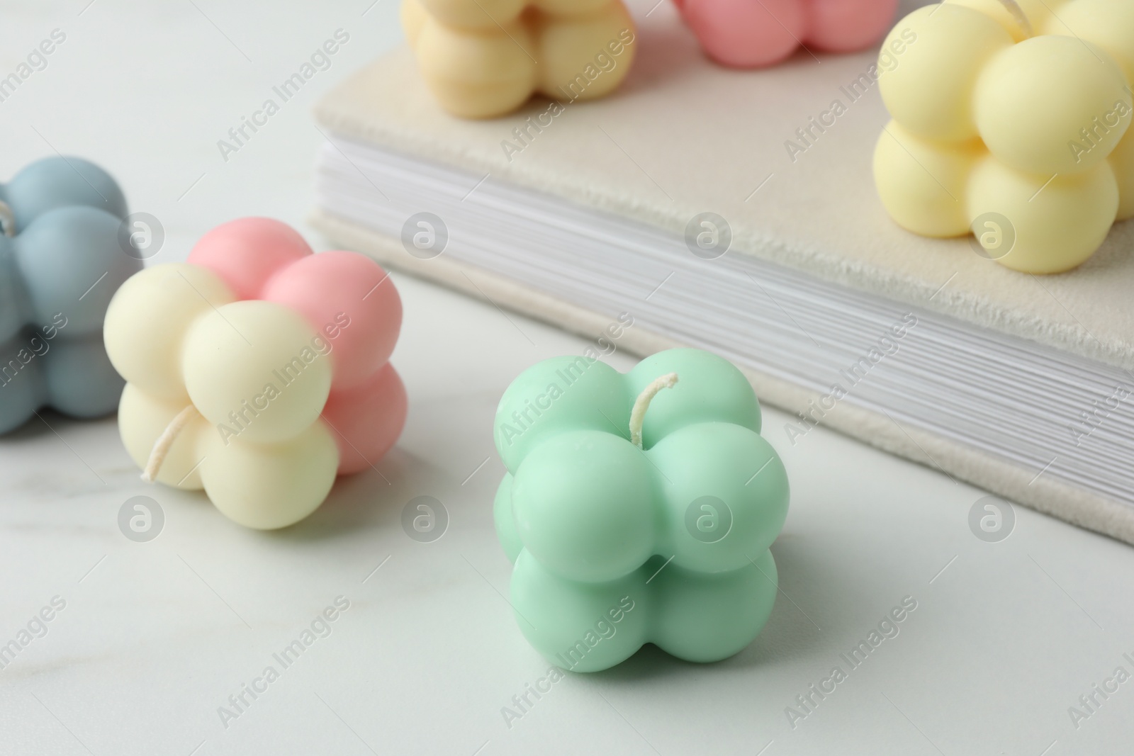 Photo of Different stylish bubble candles and book on white table, closeup