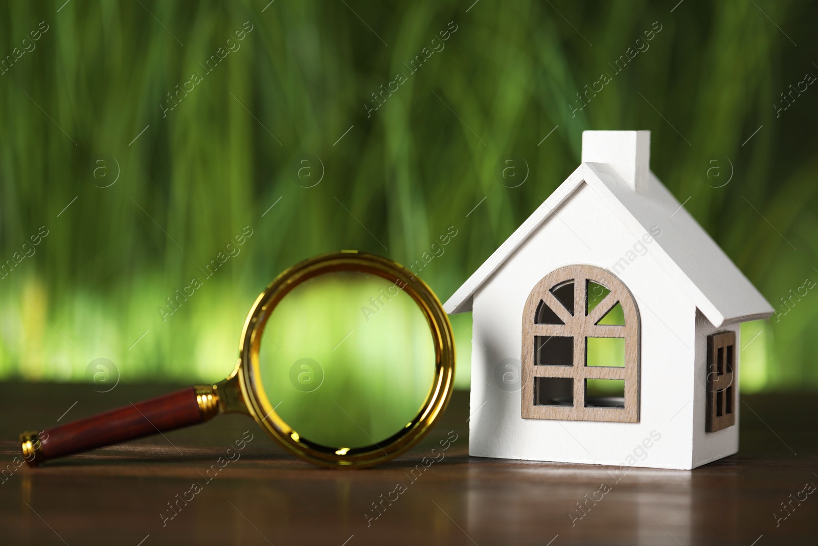 Photo of House hunting. Magnifying glass and house figure on wooden table